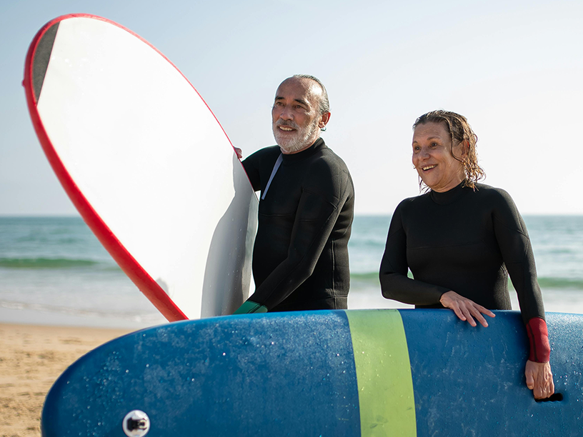 Older couple on the beach holding surfboards