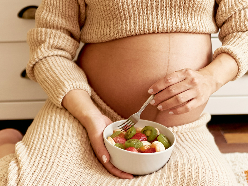 Pregnant woman eating bowl of fruit