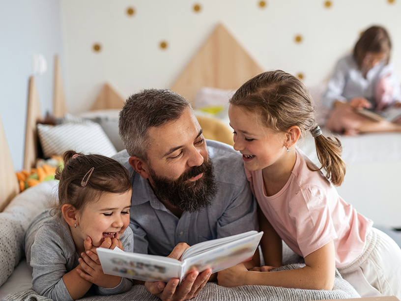 Father laying down and reading to two young daughters